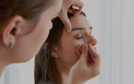 Beauty technician shaping a client’s eyebrows using tweezers
