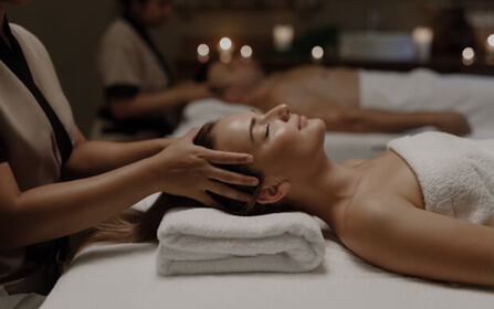 Woman relaxing with her eyes closed while wearing a white robe and head towel in a spa setting
